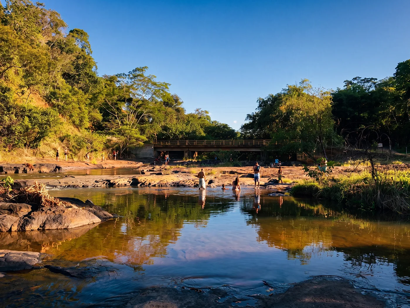 O Rio Pirapetinga: as pedras, a água baixa e a ponte de concreto ao fundo